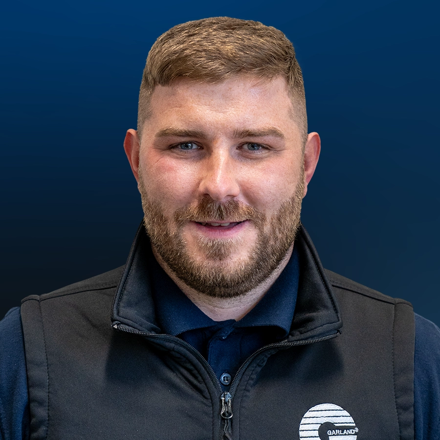 Professional headshot of Josh Wall wearing black Garland vest over blue shirt