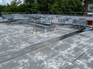 Flat commercial rooftop with aging, cracked waterproof membrane and various HVAC ducts and vents visible across the surface.