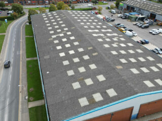 Wide drone shot of the original industrial roof system prior to refurbishment, showing extensive wear, staining and degraded translucent rooflights.