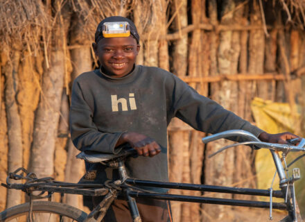 Child with solar powered head lamp smiles with his bicycle.