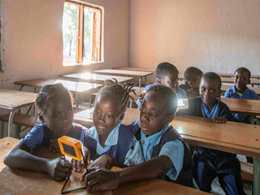 Children in a classroom in Zambia using small solar-powered lights on their desks while studying together.