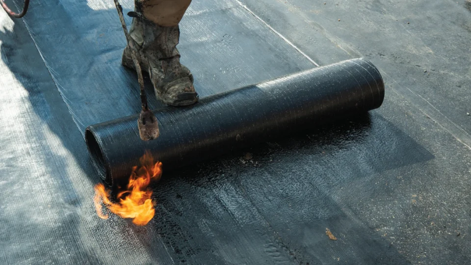 Worker using torch to heat asphalt roofing membrane during installation