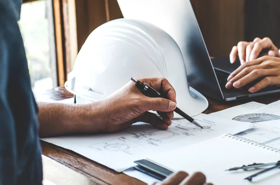Architect reviewing construction blueprints with hard hat and laptop
