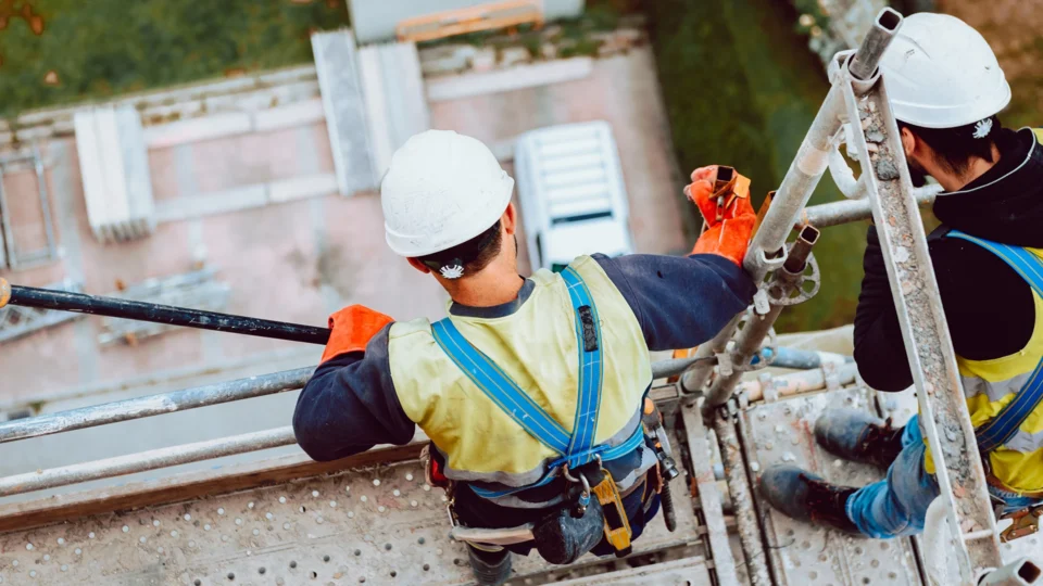 Construction workers wearing safety harnesses climbing metal scaffolding on building site