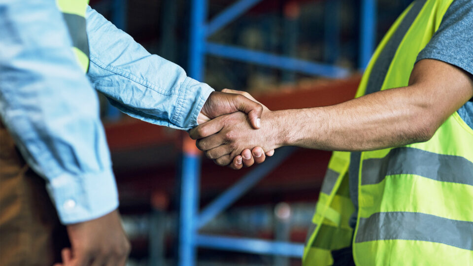 Two workers shaking hands at industrial warehouse facility outdoors