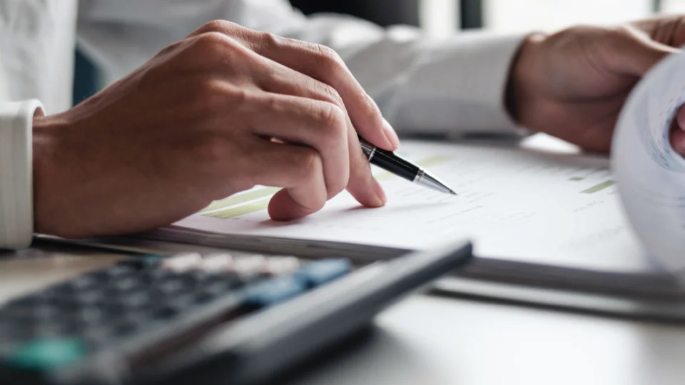Person pointing with pen at budget tracking document with calculator nearby