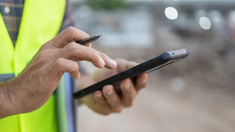 Worker in safety vest using stylus on digital tablet outdoors