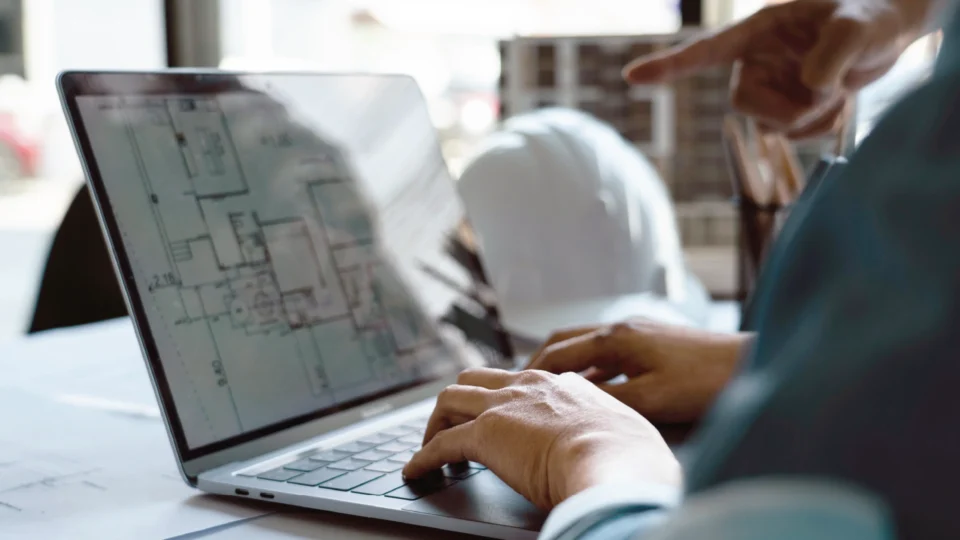 Construction professionals reviewing architectural blueprints on laptop computer together