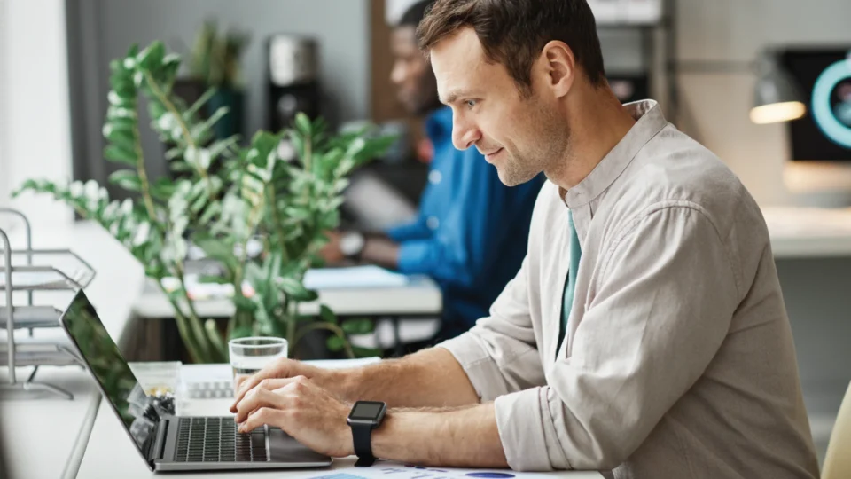 Professional man working on laptop at modern office desk with plant