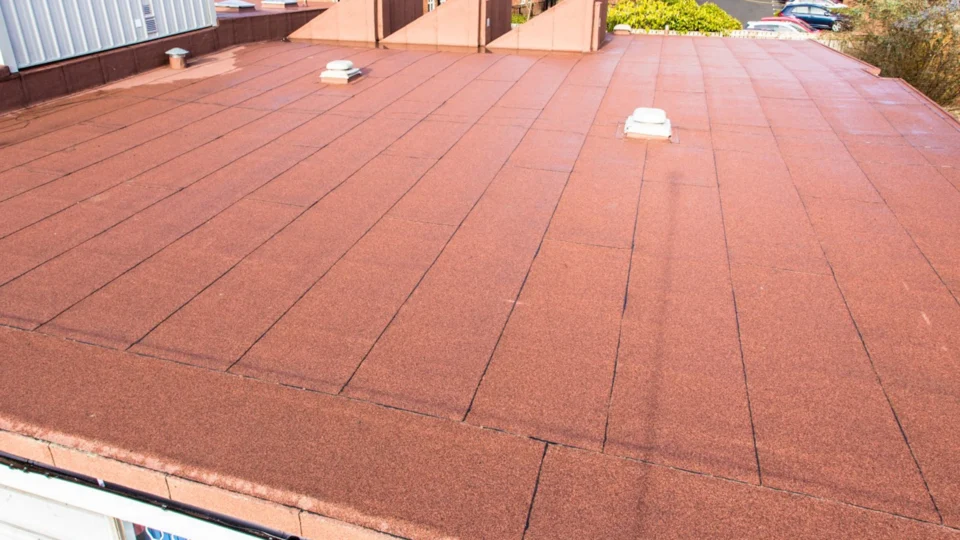 Red asphalt shingle roof with ventilation caps and seams visible