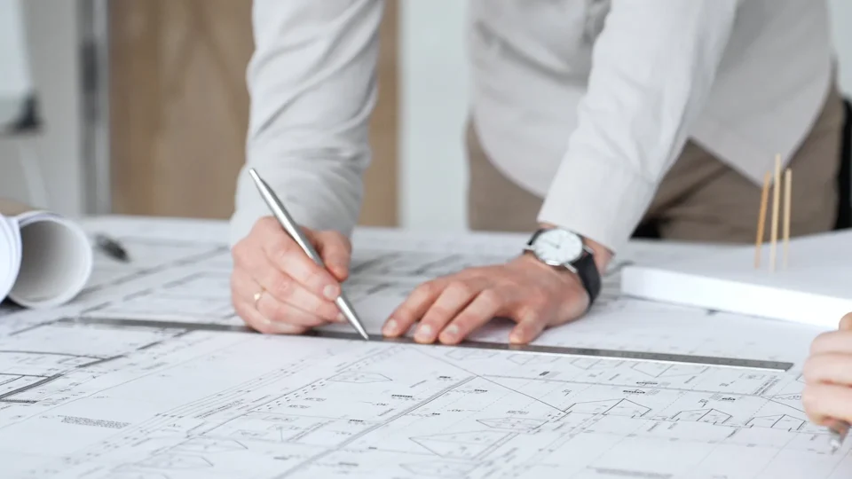 Architect reviewing building blueprints with pen at desk