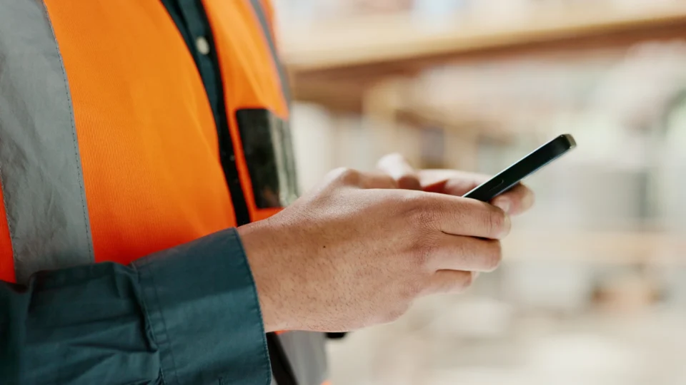Construction worker in orange safety vest holding mobile phone on job site