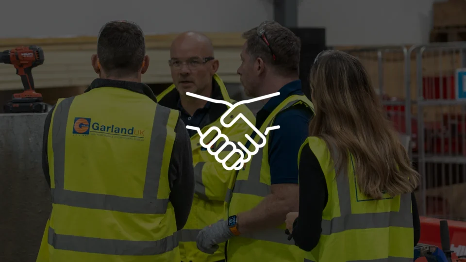 Garland UK employees in high-visibility vests shaking hands together indoors