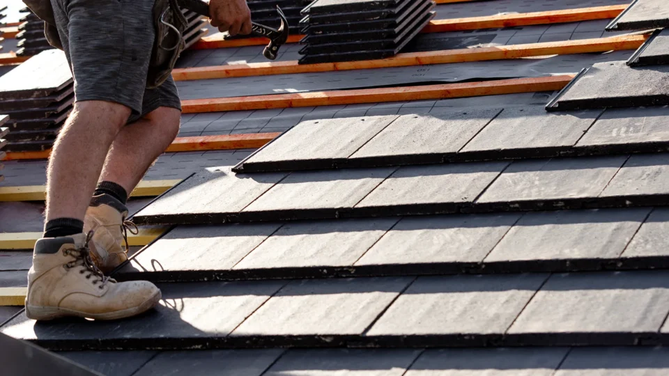 Roofer installing slate tiles on residential roof structure
