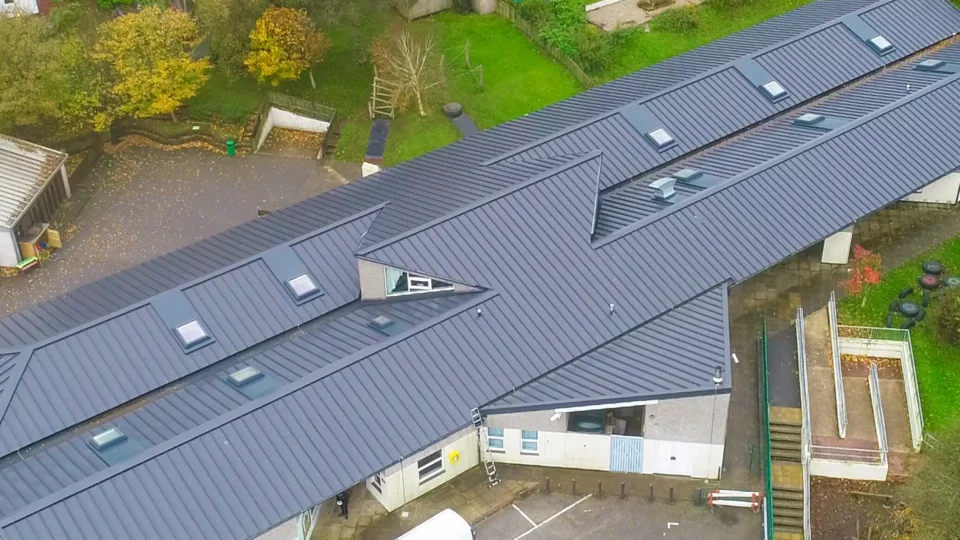 Aerial view of modern school building with dark metal roof and skylights