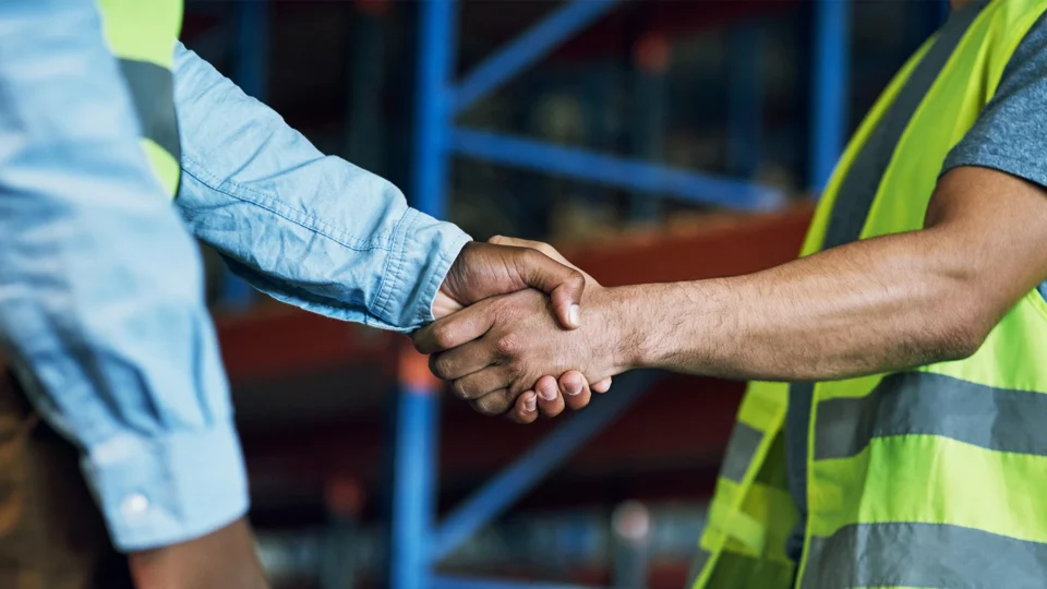 Two workers shaking hands at industrial warehouse site