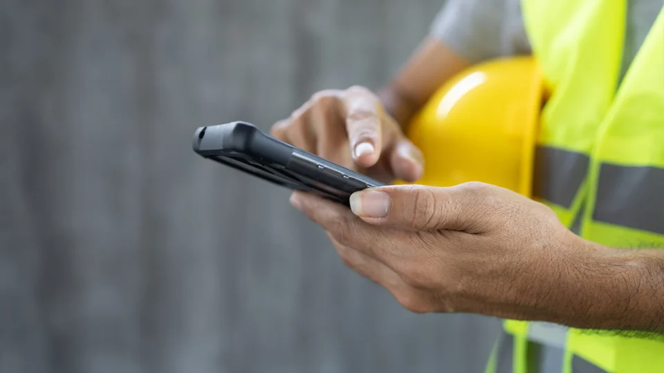 Construction worker in safety vest holding mobile device outdoors