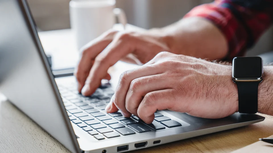 Man typing on laptop keyboard wearing smartwatch at desk