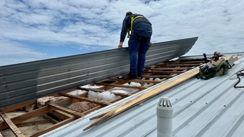 Worker installing metal roofing panels on residential structure during construction.