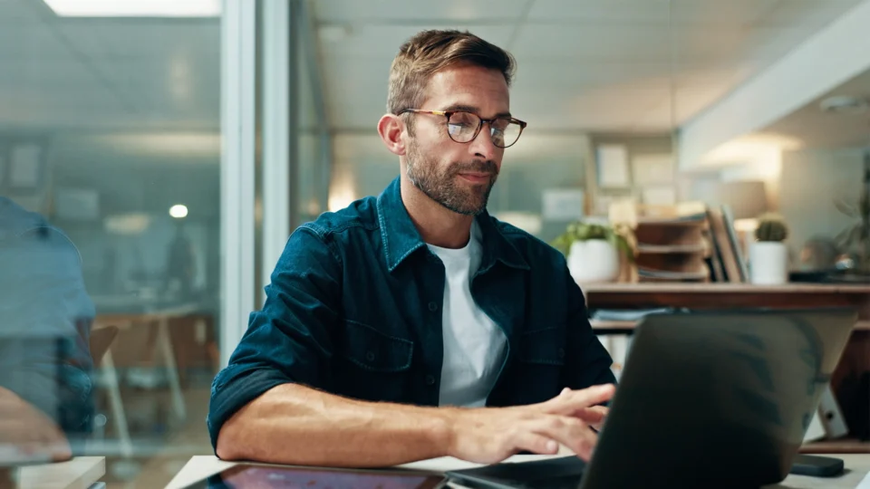 Man wearing glasses working on laptop at modern office desk
