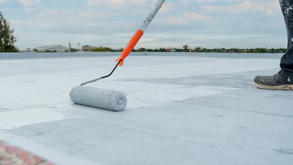 Worker applying protective coating to flat roof surface with roller