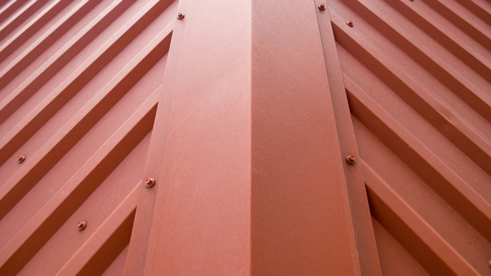 Close-up of pink corrugated metal roof panels with fasteners and shadows