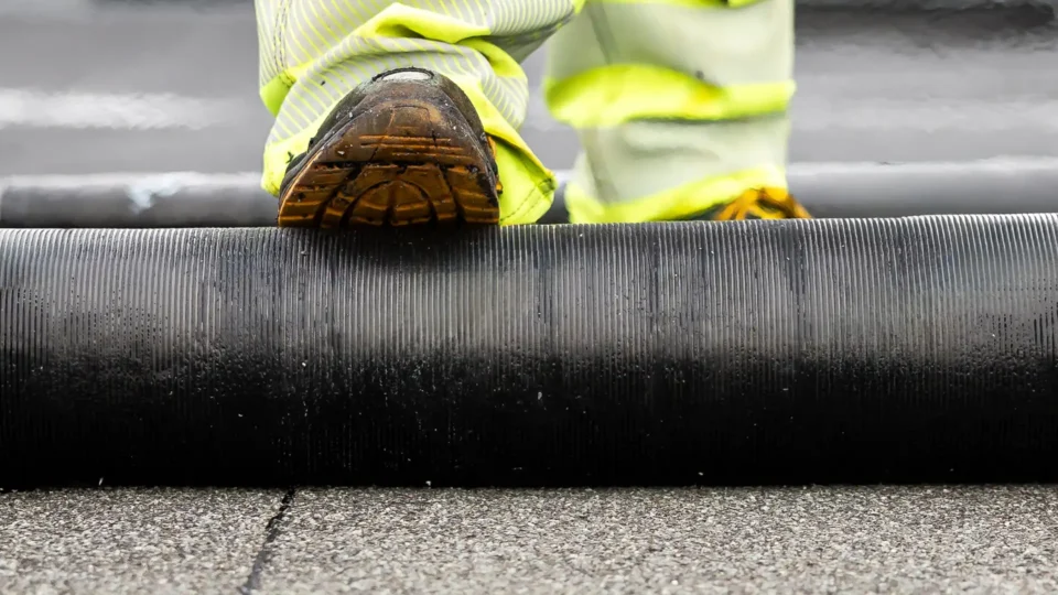 Worker in safety boots installing textured asphalt roofing material