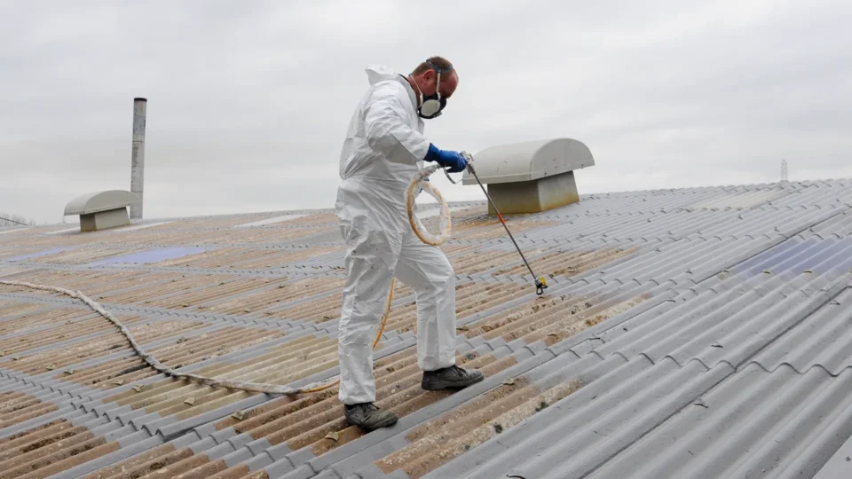 Worker in white protective suit spraying asbestos roof material removal